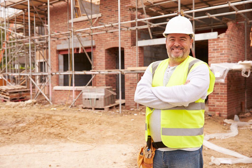 Construction worker smiling with arms folded across his chest at Building Site