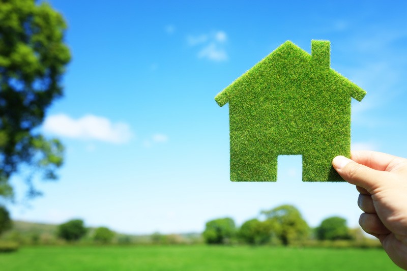 Cut out house made of grass held up to a blue sky background.