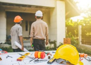 Contractors with tools in backdrop communicating about home construction plans.