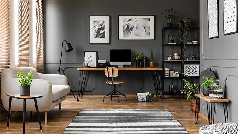 Posters on grey wall above wooden desk with computer monitor in modern home office interior with plants