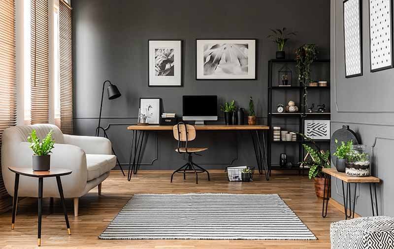 Posters on grey wall above wooden desk with computer monitor in modern home office interior with plants