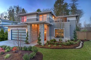 Two story Contemporary style home at dusk with stone details, wood siding, large windows, and a balcony.