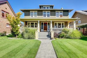 Two story craftsman style home with covered porch and clean lawn in daytime.