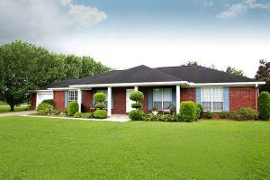 Ranch style home with brick detailing, covered porch, and expansive clean lawn.