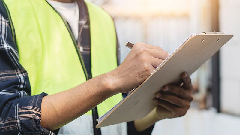 Man in safety vest writing on clipboard to avoid construction mistakes