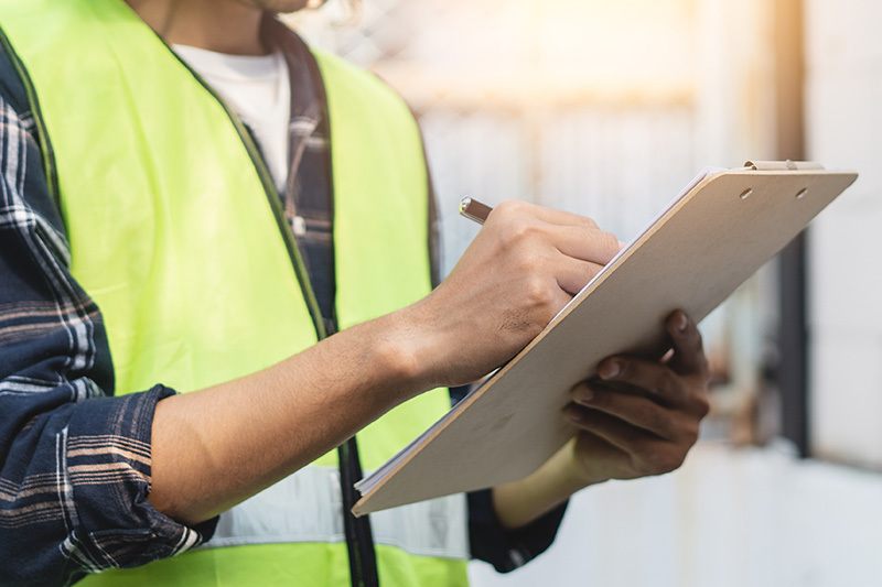 Man in safety vest writing on clipboard to avoid construction mistakes