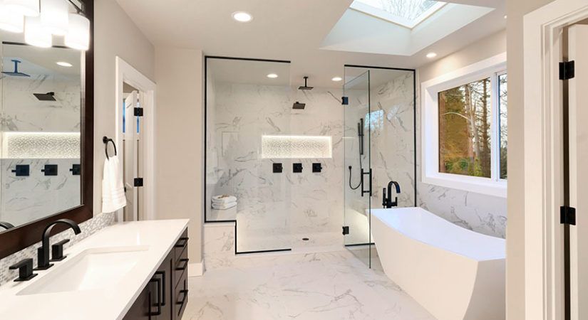 Luxury modern home bathroom interior with dark brown cabinets, white marble, walk in shower, free standing tub, two mirrors, flowers.