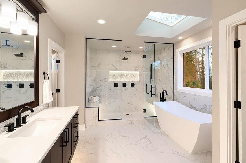 Luxury modern home bathroom interior with dark brown cabinets, white marble, walk in shower, free standing tub, two mirrors, flowers.