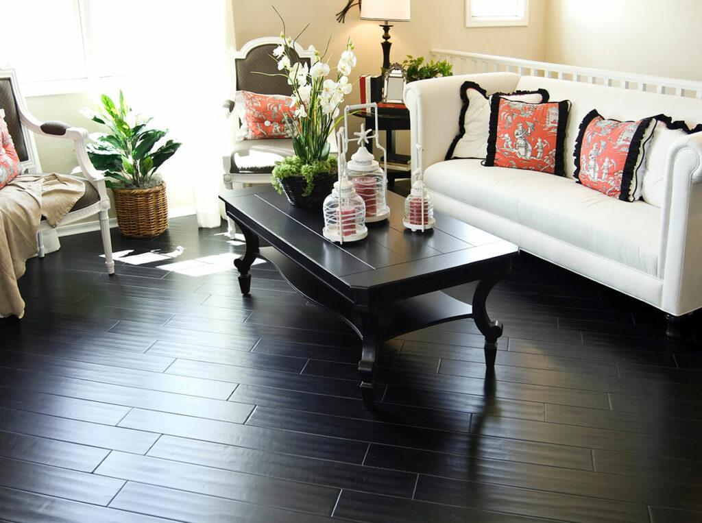 Dark hard wood floor in living room with dark coffee table, white couch and, red accents.