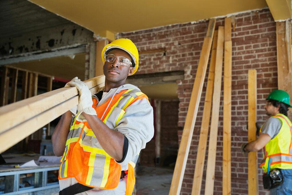 construction workers on interior job site carrying lumber