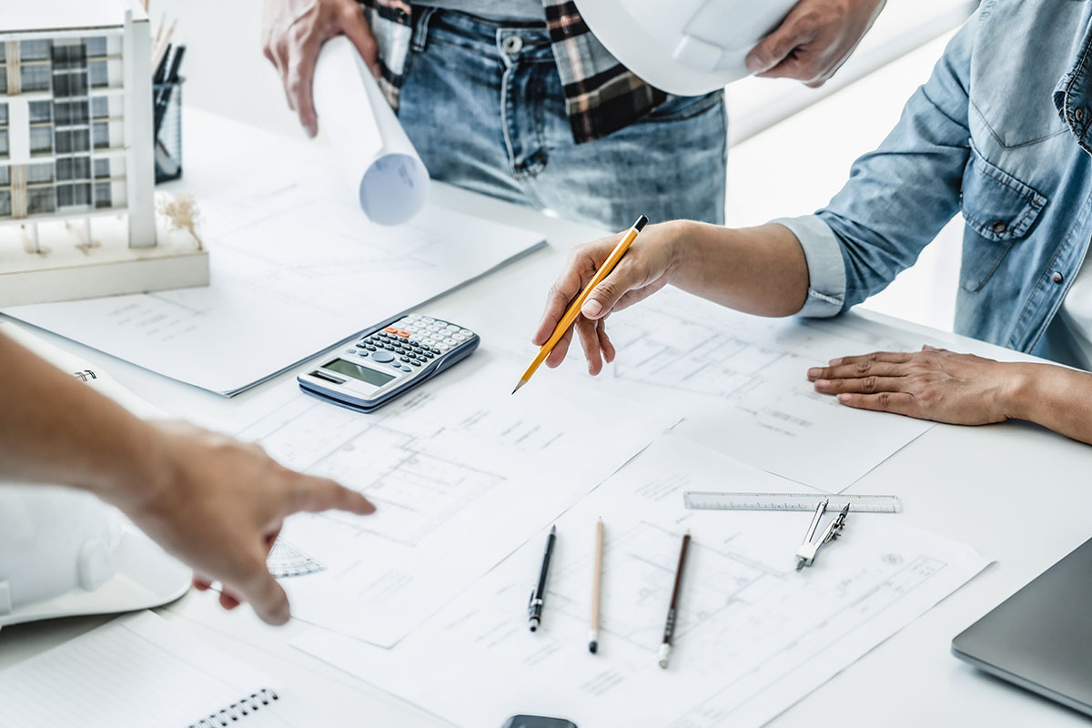 A group of architects stand around a table, planning designs for office tenant improvement projects.