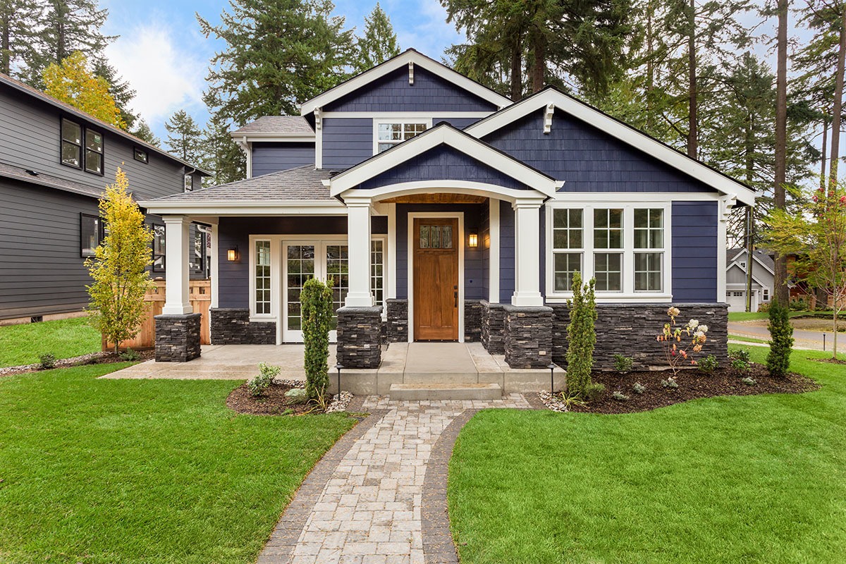 A newly constructed custom-built house with a blue exterior and a green lawn.