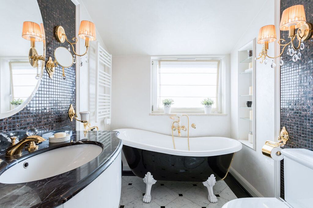 A historic-style bathroom in a new home build features a vintage black clawfoot tub, black and white tile, and antique wall sconces.