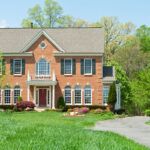 A Colonial Style new home build that looks historic, with a brick exterior, large lawn, and curvy driveway.