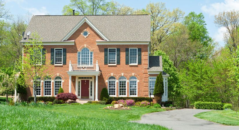 A Colonial Style new home build that looks historic, with a brick exterior, large lawn, and curvy driveway.