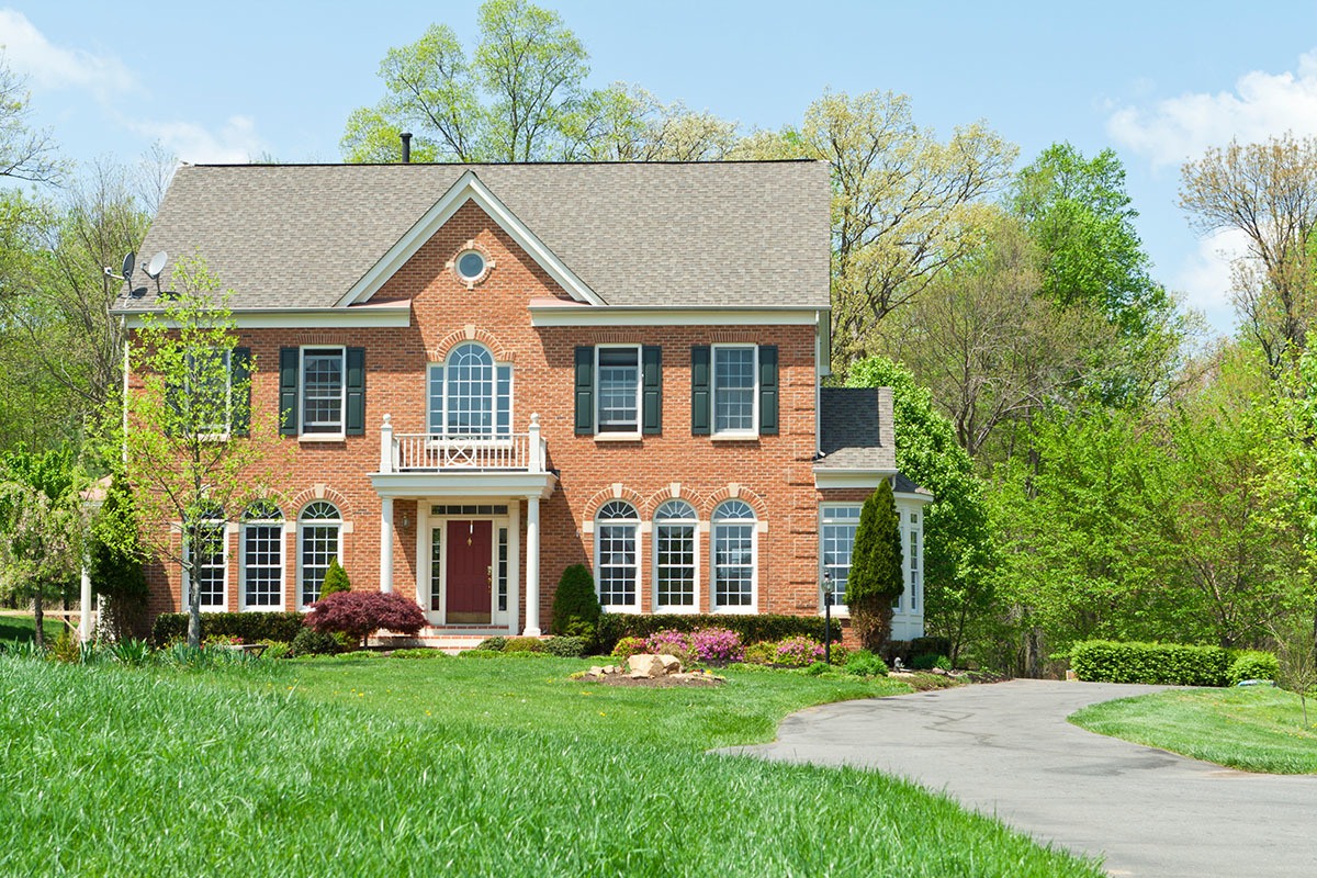 A Colonial Style new home build that looks historic, with a brick exterior, large lawn, and curvy driveway.