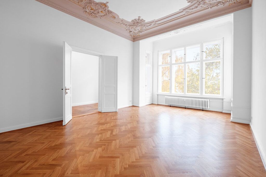 An empty room in a historic-style new home build displays parquet flooring and intricate crown molding.