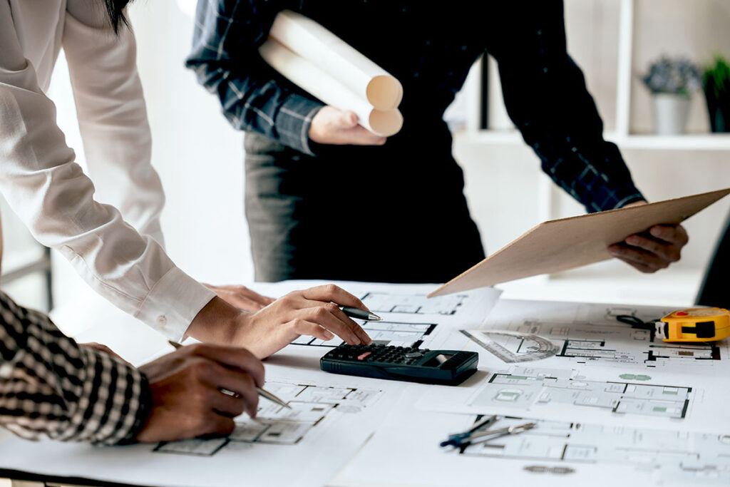 A close up of hands as a group of people go over commercial remodeling permits and other important documents at a desk.