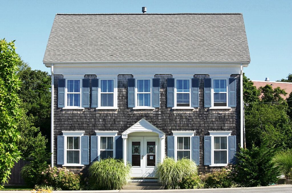 A cape cod style new home build with gray walls, surrounded by trees.