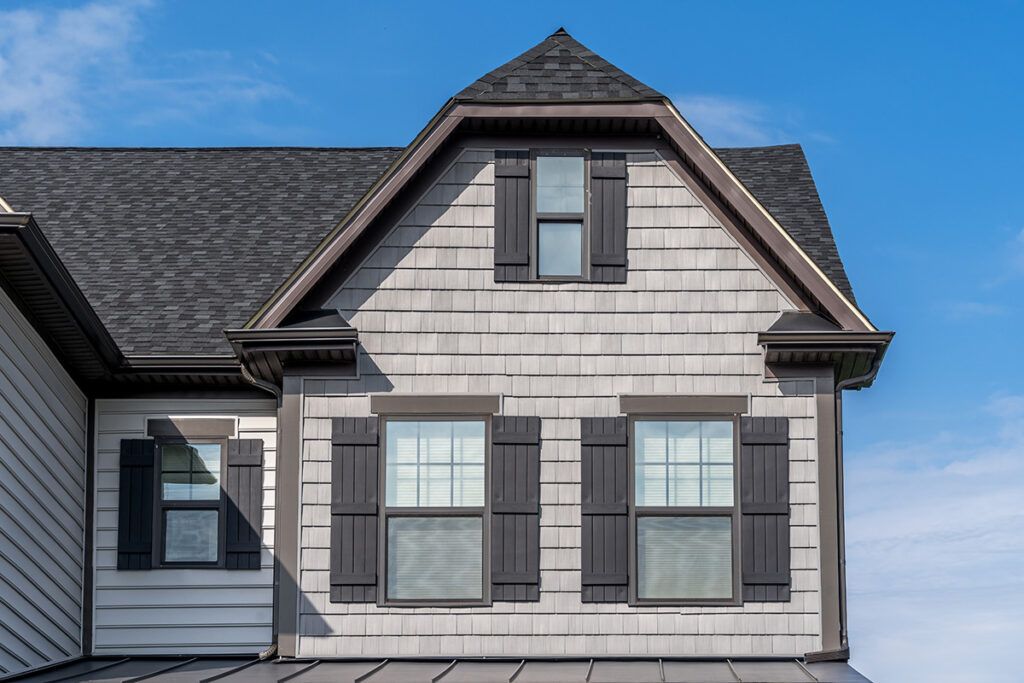 A house with dutch colonial architectural design, with a gray exterior and black trim against a blue sky