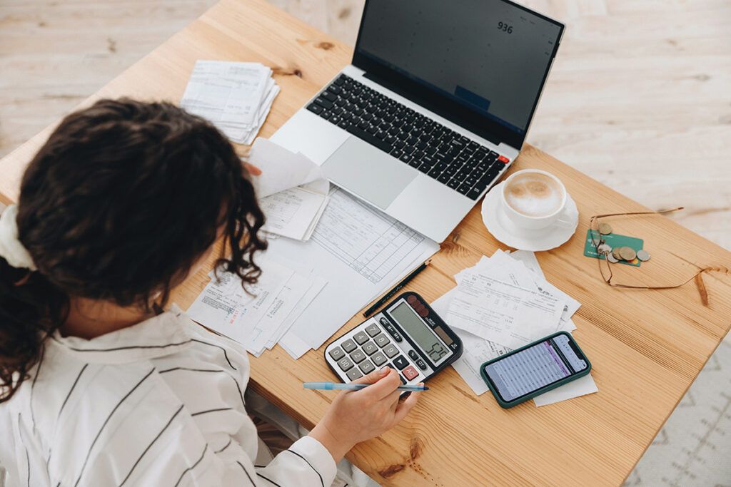 A woman sitting at a desk with a laptop and calculator, calculating utility costs for her office.