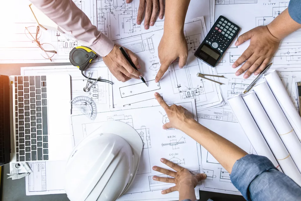 A group of hands pointing at blueprints and calculators on a table