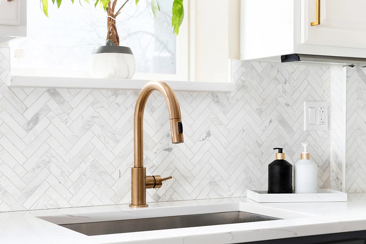 A bronze low flow kitchen sink faucet in a newly renovated kitchen with white marble countertops