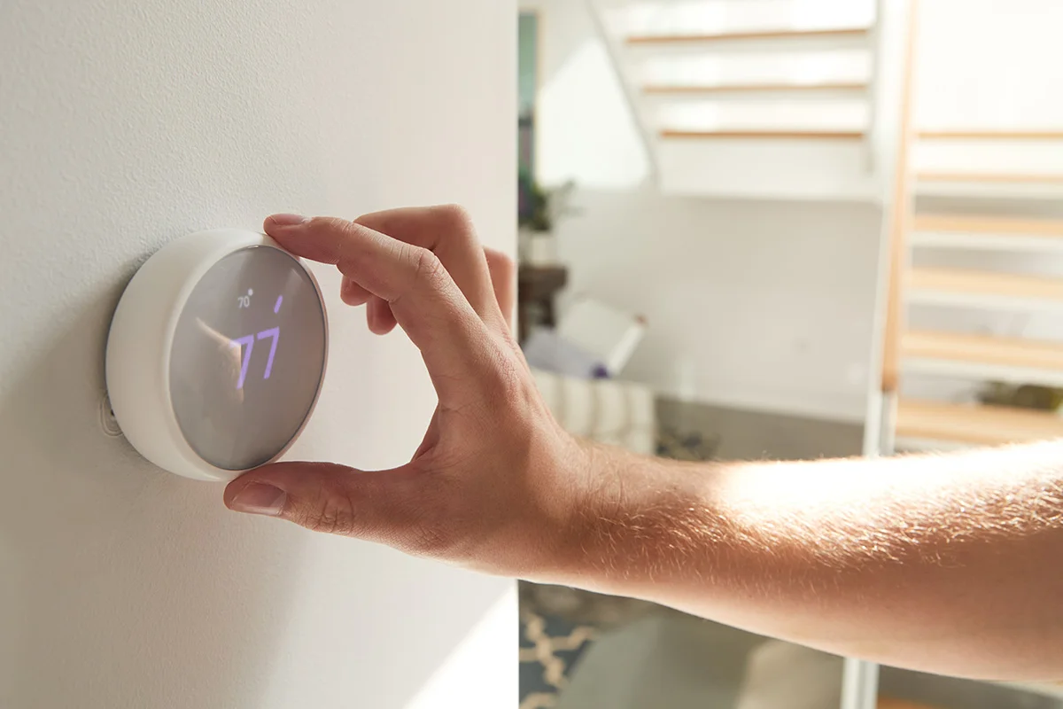 a hand adjusting a round smart thermostat, showing the concept of eco-friendly home renovations that save money