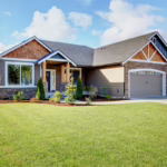 The exterior of a house with gray paint, white trim, wood accents, and a large front lawn, showing the concept of whether it's better to remodel or buy a new home