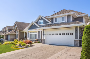 The exterior of a blue house with a white garage, large driveway, stone details, and neat landscaping, showing the concept of home renovations for building equity
