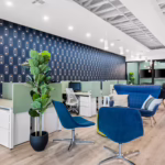 Large coworking area with blue seats and planters in a bright, well lit office space