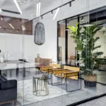 The interior of a modern commercial office space with glass wall partitions, live plants, white walls, and cement floors